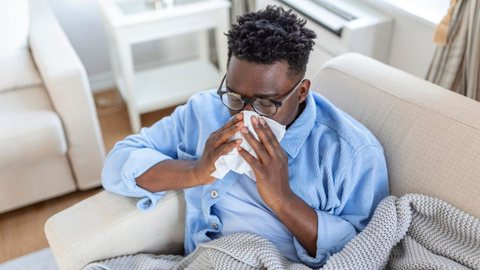 Homem com gripe assoando o nariz