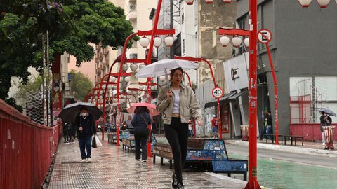 Pedestres se protegem da chuva no bairro da Liberdade - Imagem: Reprodução / Agência Brasil / Rovena Rosa