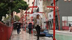 Pedestres se protegem da chuva no bairro da Liberdade - Imagem: Reprodução / Agência Brasil / Rovena Rosa