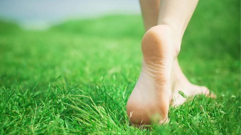 Pessoa andando descalço na grama - Imagem: Shutterstock