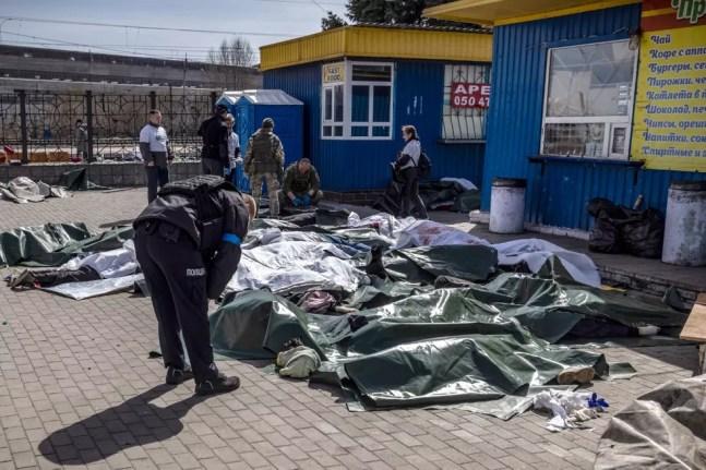 Policial ucraniano observa corpos cobertos após ataque russo a estação de trem em Kramatorsk, usada como rota de evacuação para civis — Foto: FADEL SENNA / AFP