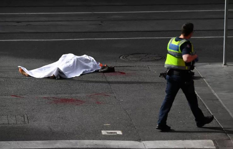 Policial caminha perto do corpo de vítima de ataque no centro de Melbourne, na Austrália, nesta sexta-feira (9)  — Foto: AAP/James Ross/via Reuters