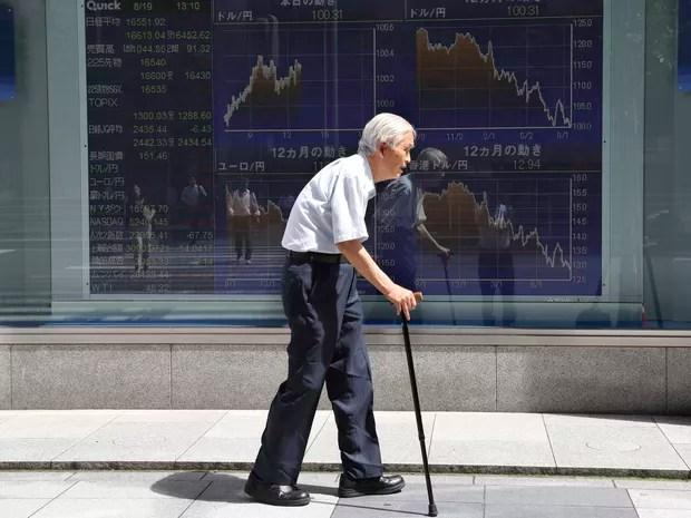 Idoso passa em frente a cotações do mercado financeiro em Tóquio, Japão (Foto: AP Photo/Koji Sasahara)