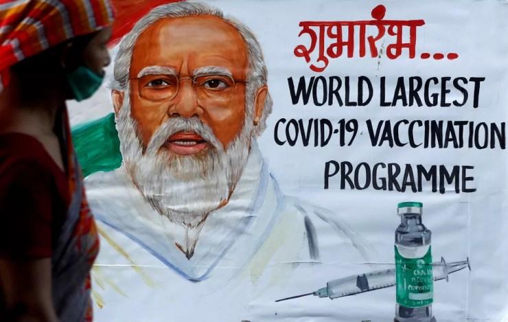 Uma mulher passa por uma pintura do primeiro-ministro indiano, Narendra Modi, em Mumbai, um dia antes da inauguração da campanha de vacinação contra a Covid-19, no dia 15 de janeiro. O cartaz diz 'maior programa de vacinação contra a Covid-19 do mundo'. — Foto: Francis Mascarenhas/Reuters