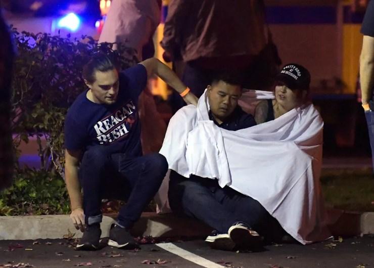 Jovens sentam em rua próxima ao bar em que tiroteio deixou mortos na noite desta quarta-feira (7) na Califórnia — Foto: Mark J. Terrill/AP Photo