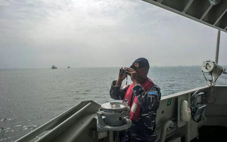 Marinheiro usa binóculos durante operação de busca de vítimas, destroços e equipamentos do avião da Lion Air nas águas de Java, na Indonésia — Foto: Fauzy Chaniago / AP