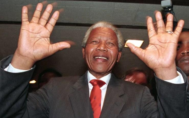 Nelson Mandela levanta as mãos enquanto anda dentro da 'Johannesburg Stock Exchange' em 22 de abril de 1994. — Foto: Corinne Dufka/Reuters