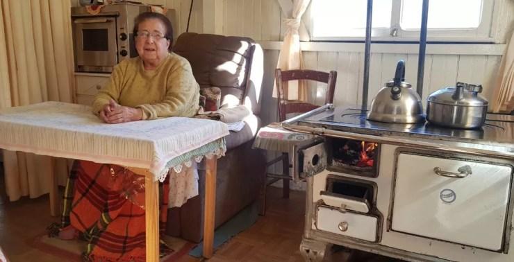 Dona Judite Souza aproveitou para ficar próximo do fogão a lenha para se proteger do frio em São Joaquim — Foto: Mycchel Hudsonn Legnaghi/São Joaquim Online
