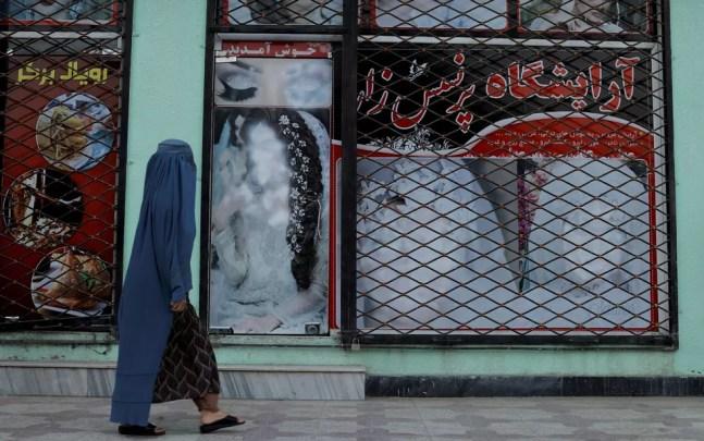 Mulher usando burca passa em frente a vitrine com imagens de modelos pintadas de branco, em Cabul, no Afeganistão, em 6 de outubro  — Foto: Reuters/Jorge Silva