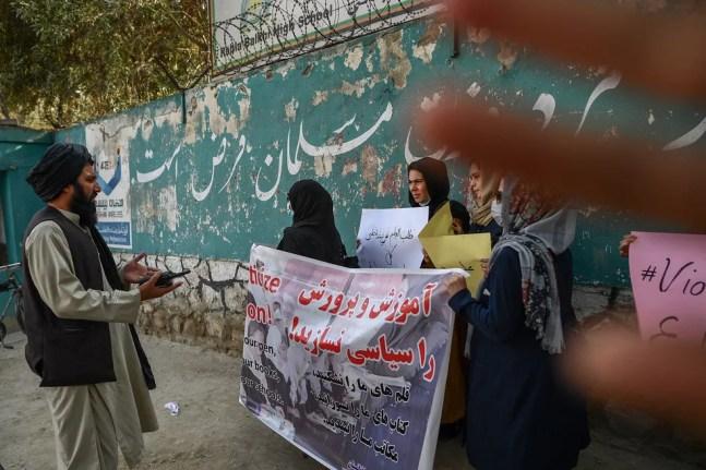 Membro do Talibã conversa com manifestantes mulheres enquanto outro tenta bloquear a visão da câmera com a mão durante protesto realizado do lado em frente a uma escola em Cabul, capital do Afeganistão, em 30 de setembro de 2021 — Foto: Bulent Kilic/AFP