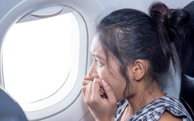 Mulher nervosa e com medo ao lado da janela do avião.