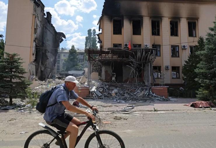Homem passa de bicicleta em frente a um prédio atingido em Lysychansk  — Foto: Alexander Ermochenko/Reuters