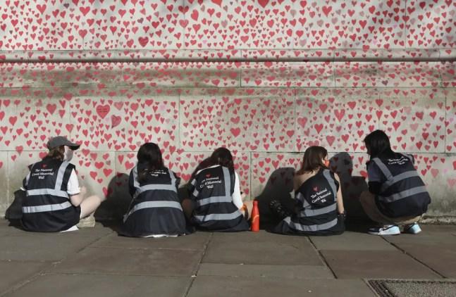 Pessoas desenham corações no National Covid Memorial Wall, que está sendo pintado em memória das pessoas que morreram de coronavírus no Reino Unido — Foto: Luciana Guerra/AP