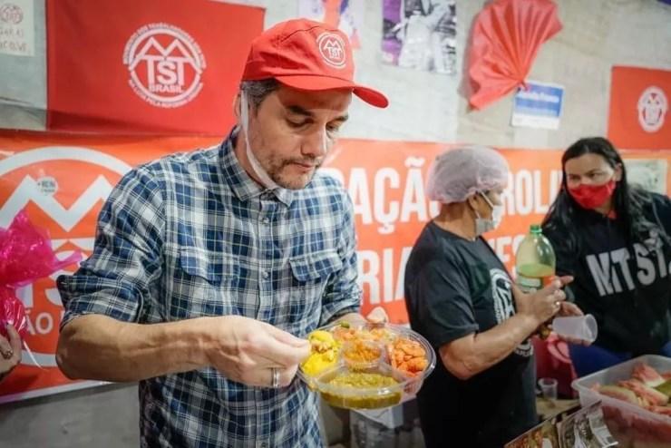 O ator Wagner Moura, diretor do filme "Mariguella", come marmita de acarajé no acampamento do MTST na Zona Leste de São Paulo na quinta-feira (11).  — Foto: Reprodução/Redes Sociais