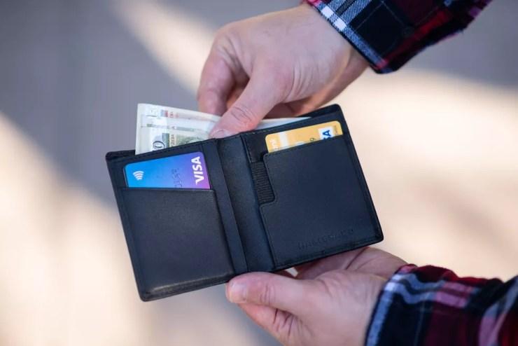 Homem mexe em carteira com cartões de crédito e dinheiro — Foto: Emil Kalibradov/Unsplash/Reprodução