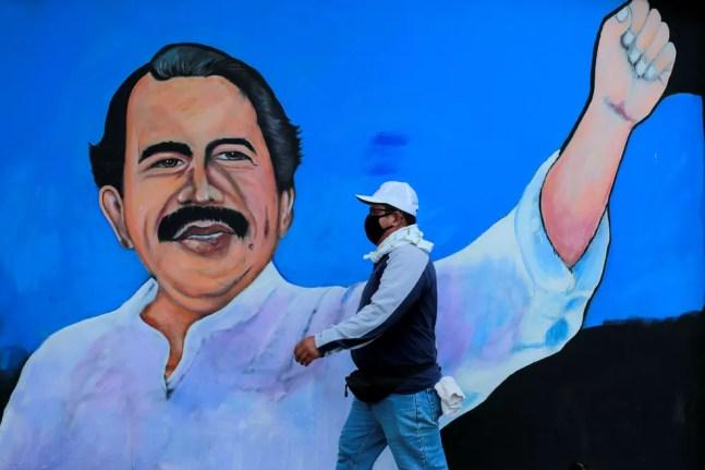 Homem com máscara caminha em frente a um muro com a figura do presidente da Nicarágua, Daniel Ortega, em 30 de março — Foto: Oswaldo Rivas/Reuters