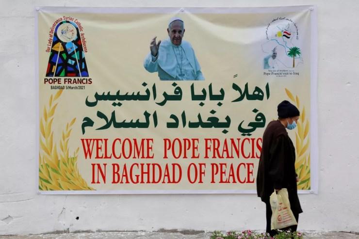 Mulher caminha perto de pôster que dá boas-vindas ao Papa Francisco em Bagdá em 4 de março  — Foto: Reuters/Teba Sadiq