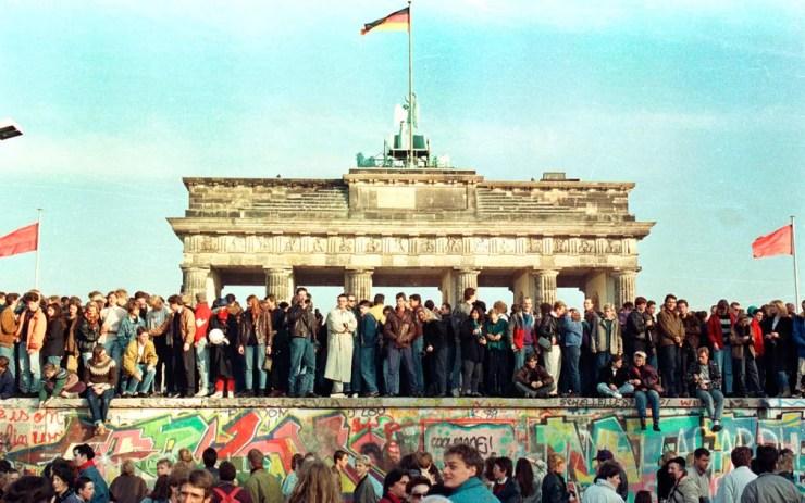 Foto de arquivo mostra cidadãos da Alemanha Ocidental ainda em vigília em cima do Muro de Berlim em frente ao Portão de Brandemburgo na manhã do dia seguinte à queda, em 10 de novembro de 1989 — Foto: Arquivo/Reuters