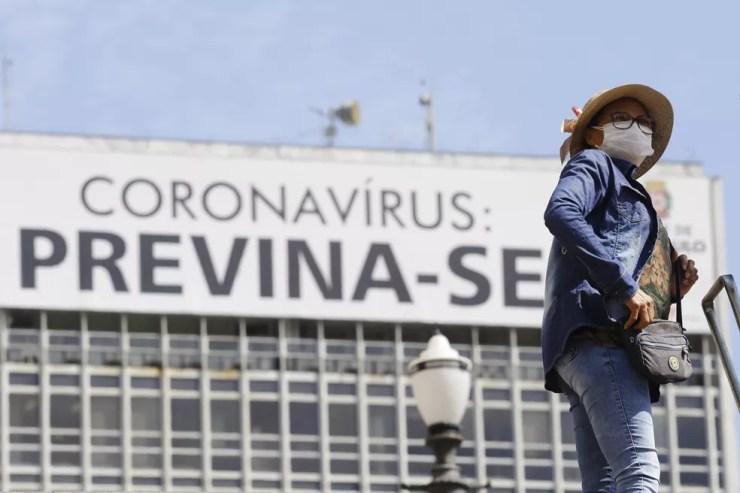 Mulher usando máscara de proteção facial passa diante de um cartaz com alerta sobre o coronavírus na região central de São Paulo, na manhã desta segunda-feira, 15 — Foto: NELSON ANTOINE/ESTADÃO CONTEÚDO