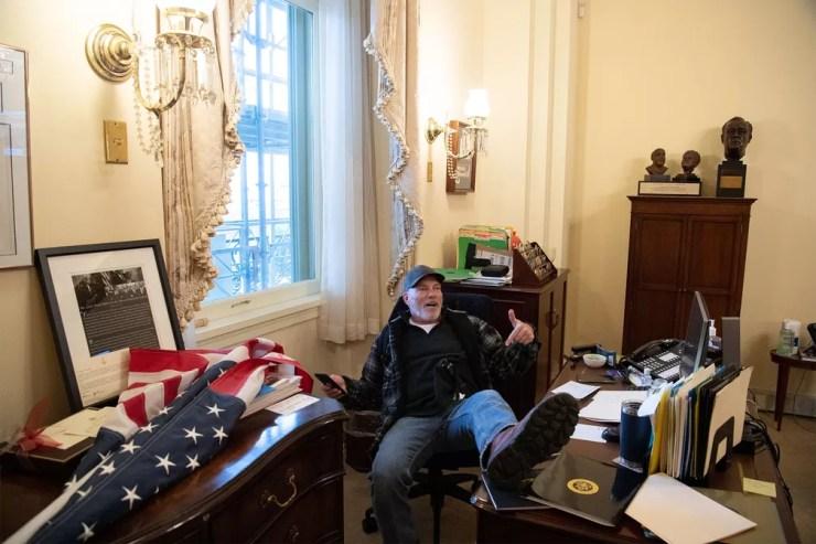 Apoiador de Donald Trump posa sentado na cadeira da parlamentar democrata Nancy Pelosi em seu gabinete no Capitólio após invasão — Foto: Saul Loeb/AFP