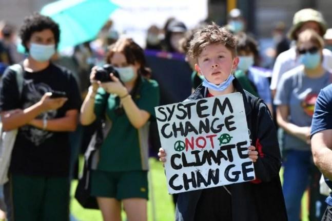 Menino com um cartaz que pede 'mudança no sistema em vez de mudança climática' — Foto: EPA via BBC