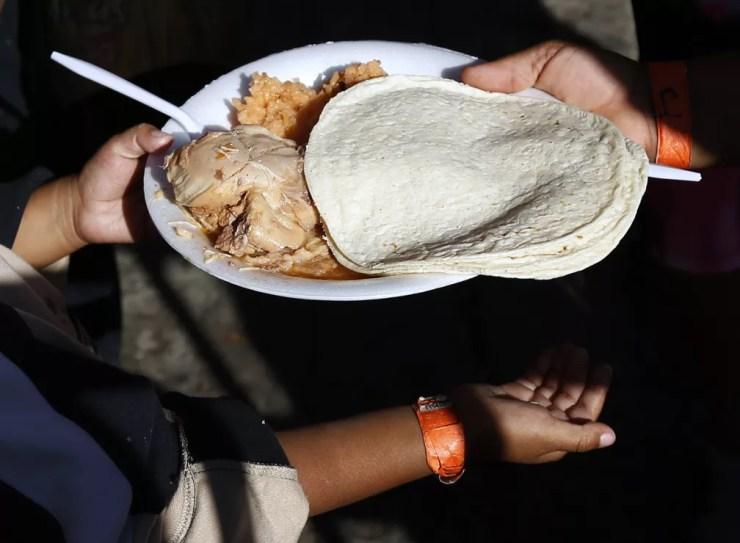 Jovem migrante recebe refeição gratuita de voluntário em abrigo em Tijuana, no México — Foto: Marco Ugarte/AP Photo