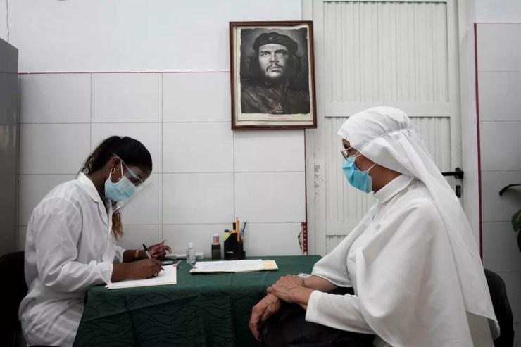 Foto mostra freira em sala de vacinação antes de receber vacina contra a Covid-19 em Havana, Cuba, no dia 23 de junho. Ao fundo, na parede, há uma foto de Che Guevara. — Foto: Alexandre Meneghini/Reuters